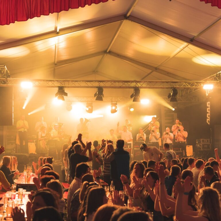 Kapelle Heilix Blechle auf der Bühne, Leute stehen auf Schrannen im Festzelt - Eventfotograf Ostalbkreis